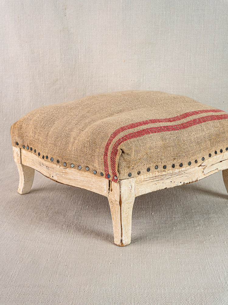 Antique French footstool with painted Louis XV frame, hemp torchon cushion, red stripes, and metal studs.