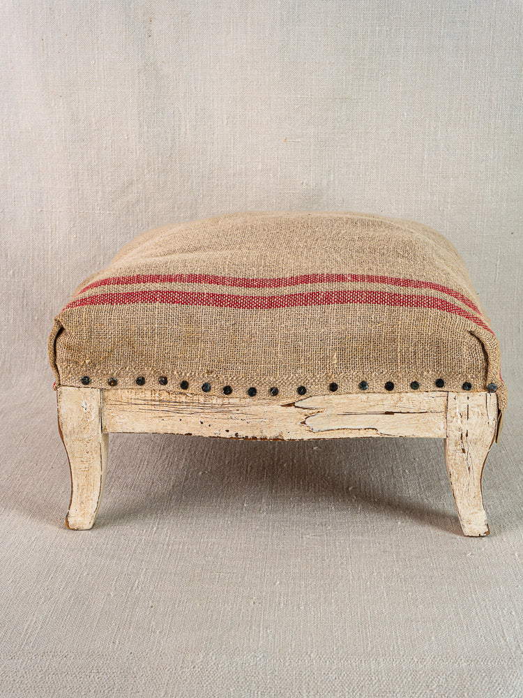 Antique French Louis XV footstool with painted frame, curved legs, hemp torchon upholstery, and red stripe.