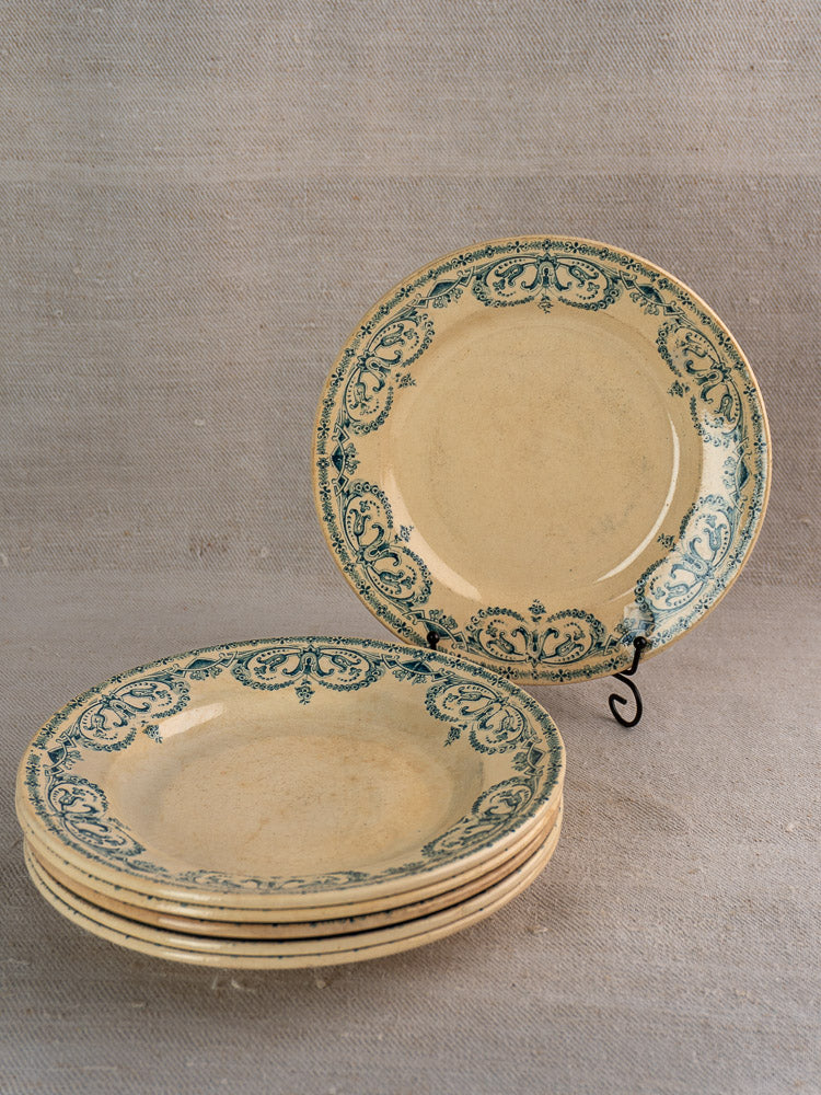 Set of six antique French Terre de Fer faience dinner plates with blue floral design, one displayed on metal stand.