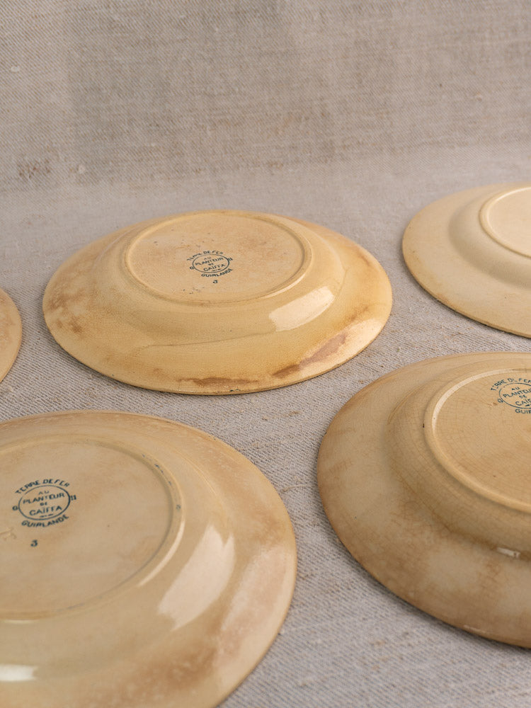 Six antique French Terre de Fer Caïffa Guirlande dinner plates upside down on beige textured fabric, showcasing green maker’s marks.
