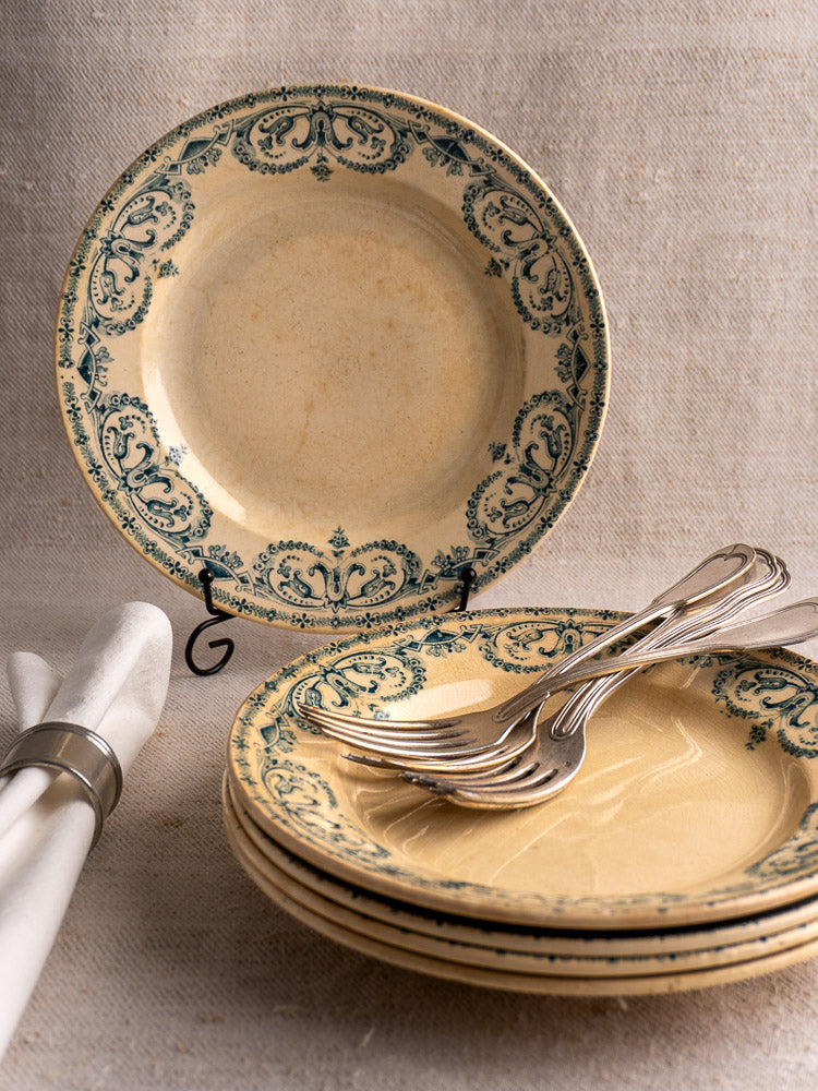 Set of six Antique French Terre de Fer Faience dinner plates with green borders, silver forks, and white napkin on beige surface.