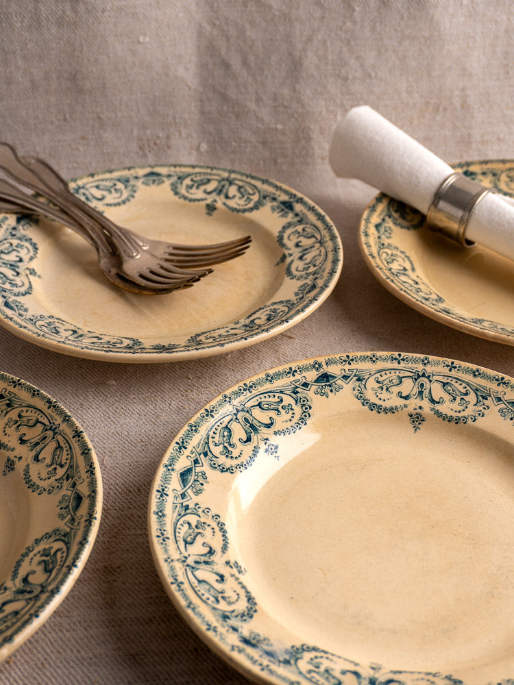 Set of six Antique French Terre de Fer Faience dinner plates with Caïffa Guirlande blue pattern on textured fabric.
