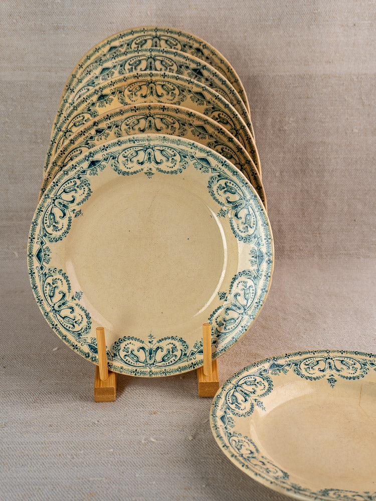 Set of six cream-colored antique French Terre de Fer faience dinner plates on wooden stand, neutral fabric backdrop.