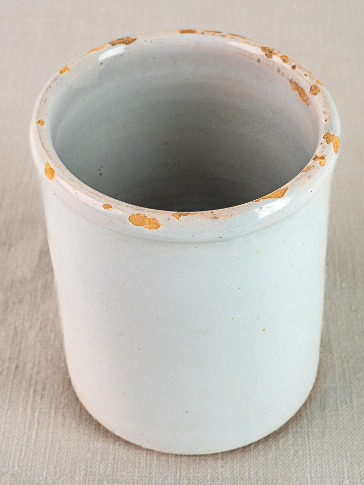 Antique white glazed French earthenware Pot à Rillettes with worn, chipped rim on light textured surface.