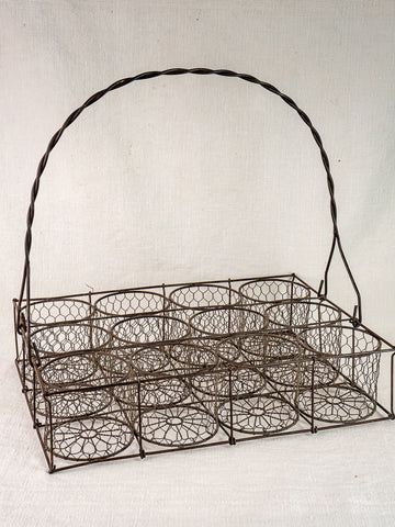Antique French wire wine carrier with twelve bottle compartments and twisted handle on neutral fabric.