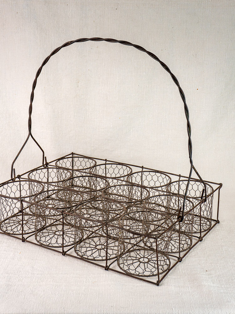 Antique French wire wine carrier with a twisted handle and 12 bottle compartments on neutral fabric.