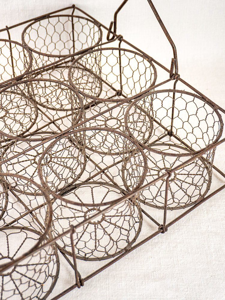 Antique French wire wine carrier with 12-bottle compartments on a light fabric surface.
