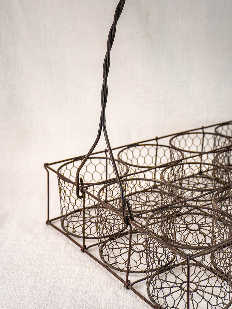 French antique wire wine carrier with twisted handle and twelve bottle compartments on neutral fabric background.