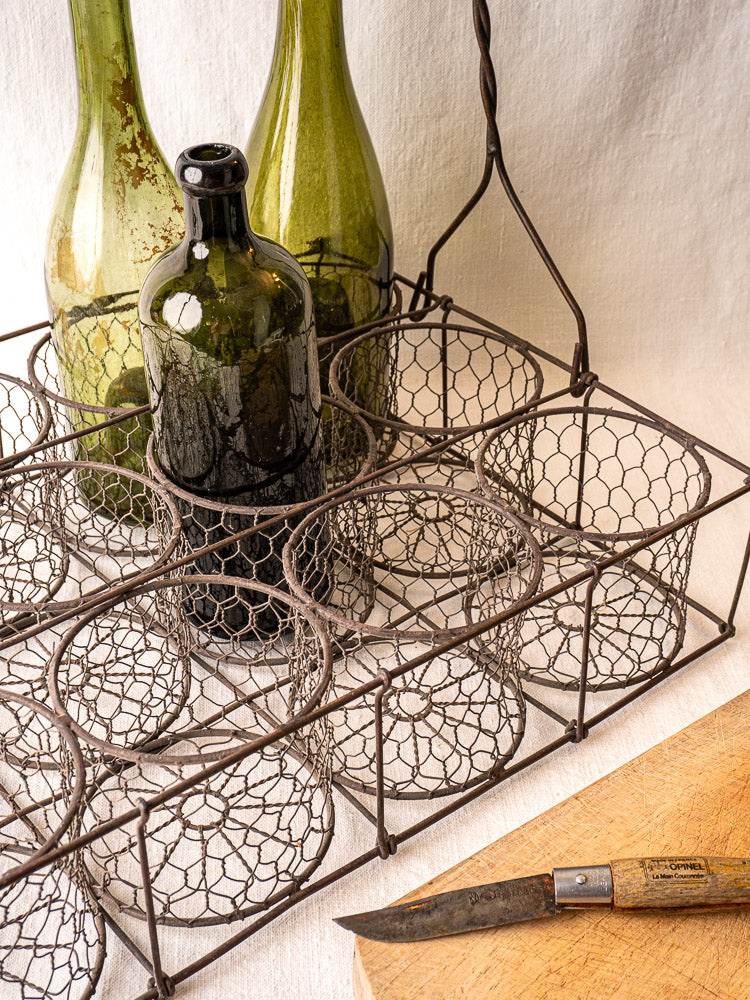 French wire wine carrier with three vintage bottles, beside a wooden-handled knife on a cutting board.