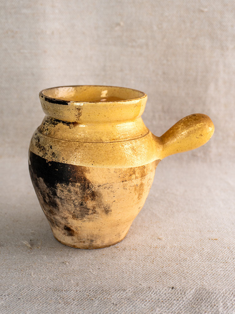 19th century French glazed terracotta toupin with side handle and weathered yellow finish on textured light fabric.