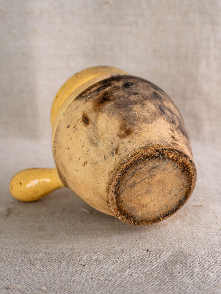 Antique French glazed terracotta toupin cooking pot with aged patina on neutral fabric background.