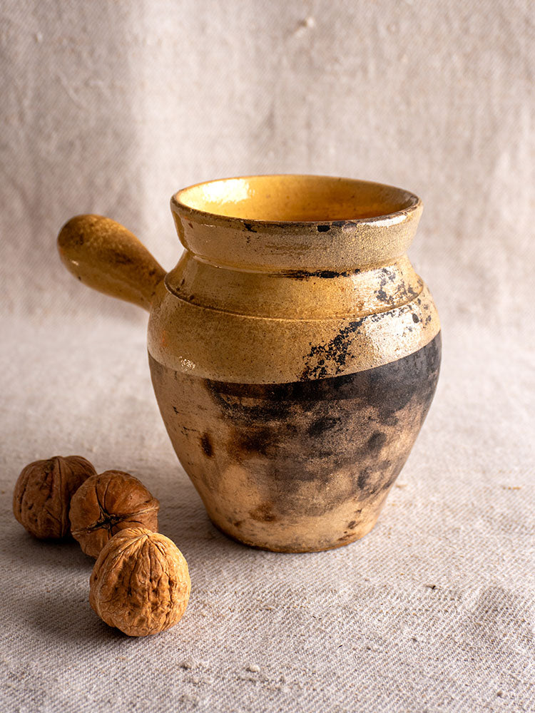 Antique French glazed terracotta toupin cooking pot on textured beige cloth next to three walnuts.