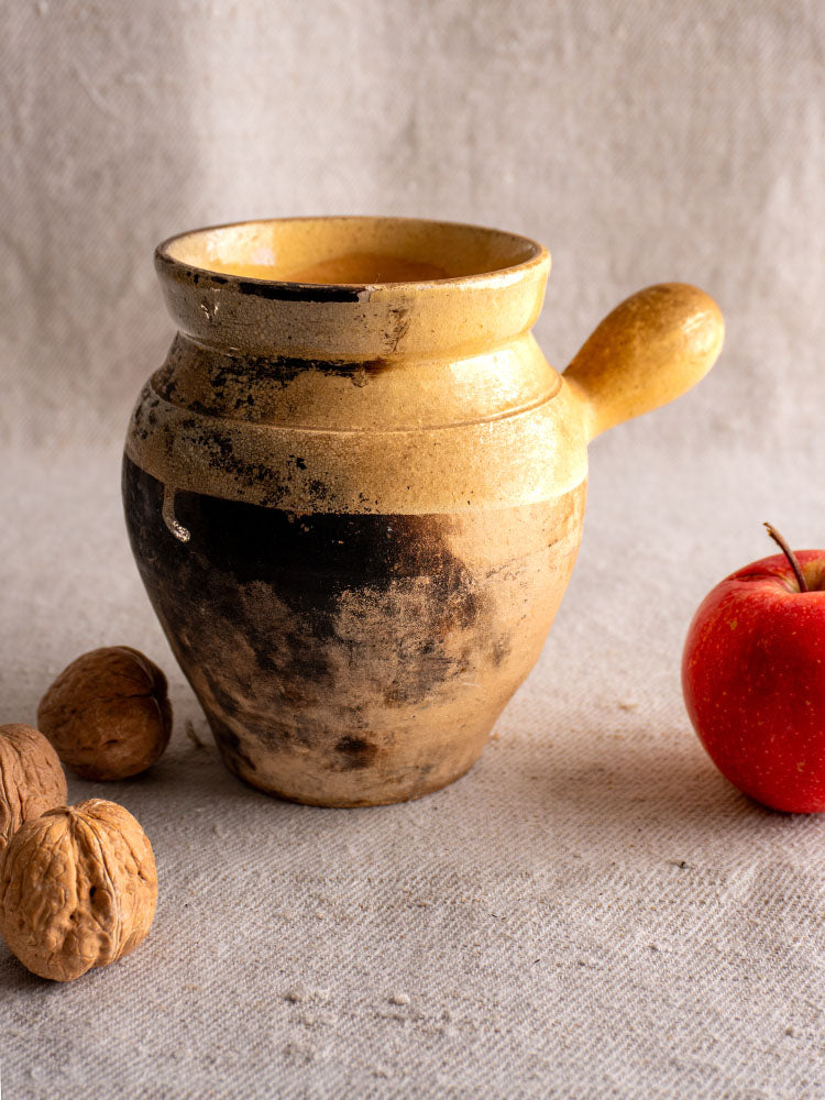 Antique French 19th-century glazed terracotta toupin with single handle and Provençal yellow and black design on beige fabric.