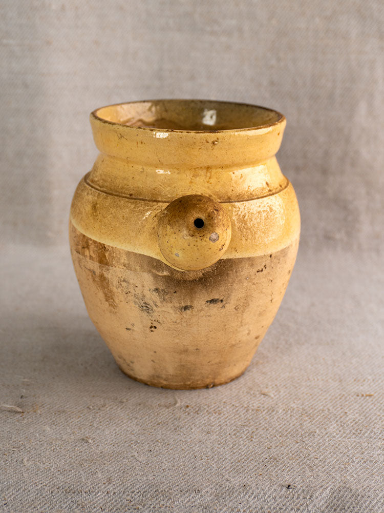Antique French toupin, 19th-century glazed terracotta with rustic yellow glaze and side spout on gray textured fabric.