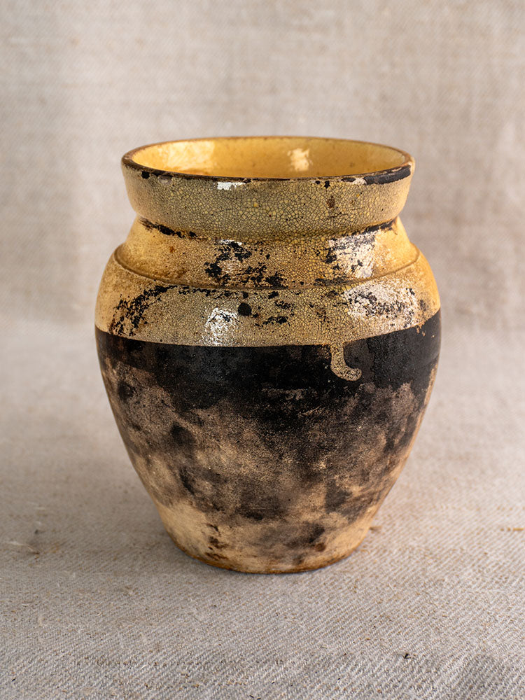 Antique French glazed terracotta toupin vase with yellow speckled top and weathered base on textured fabric.