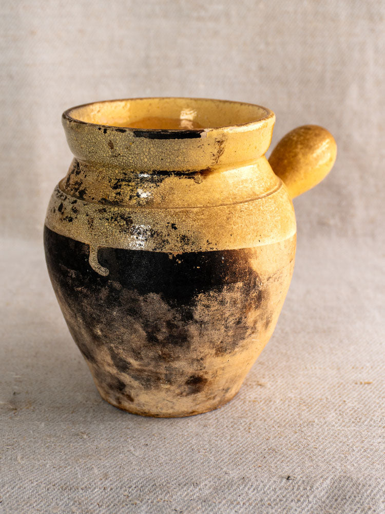19th-century French glazed terracotta toupin with yellow upper half, dark weathered base, on light textured fabric.