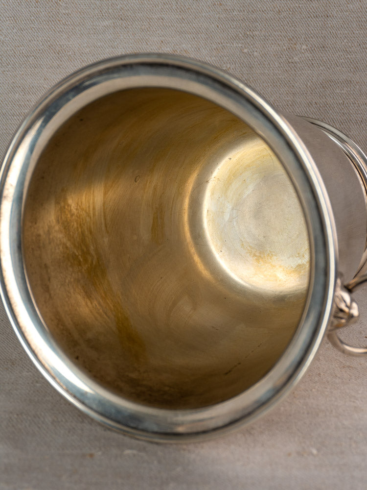 Vintage French silver-plated champagne bucket with lion head handles and gold-toned interior on beige textured surface.