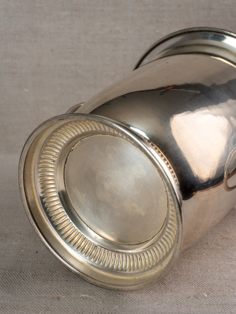 Vintage French silver plated champagne bucket with lion head handles, detailed ridged base, on beige fabric background.