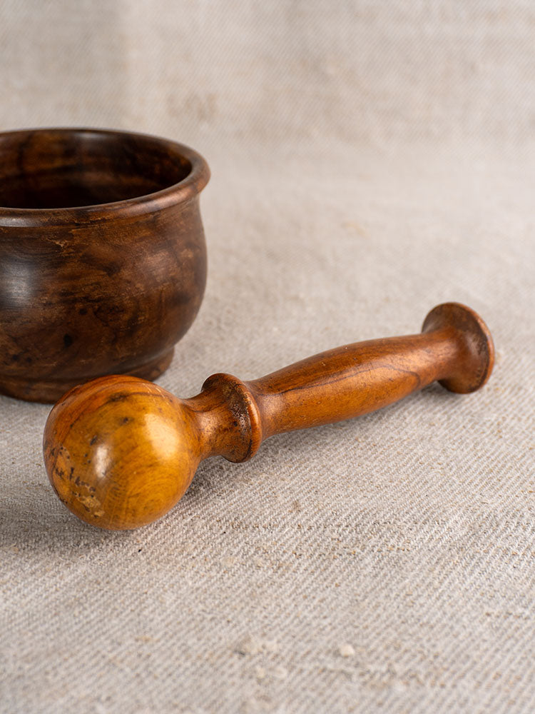 Antique French fruitwood mortar and pestle with dark bowl, light pestle, displayed on textured beige fabric.