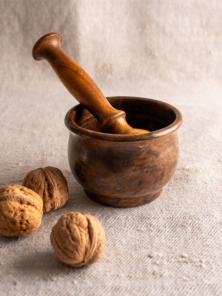 Antique French wooden mortar and pestle, hand turned, displayed on beige fabric with three walnuts.