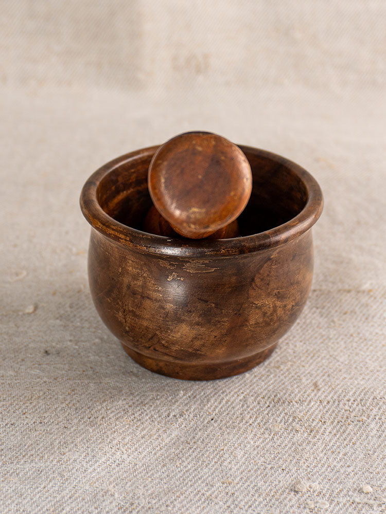 Antique French wooden mortar and pestle, hand turned, displayed on textured beige fabric.