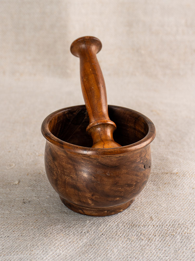 Antique French wooden mortar and pestle, hand turned, with pestle inside, displayed on textured beige fabric.