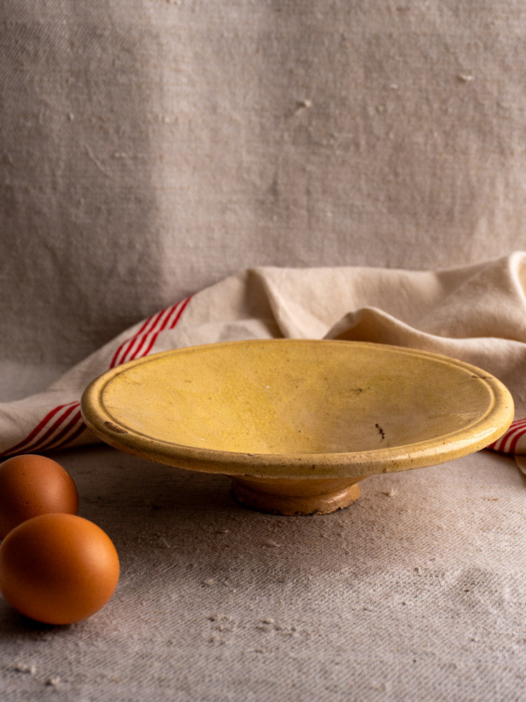 Antique French Tourne Omelette plate in Provencal yellow ochre earthenware with three brown eggs on beige cloth.