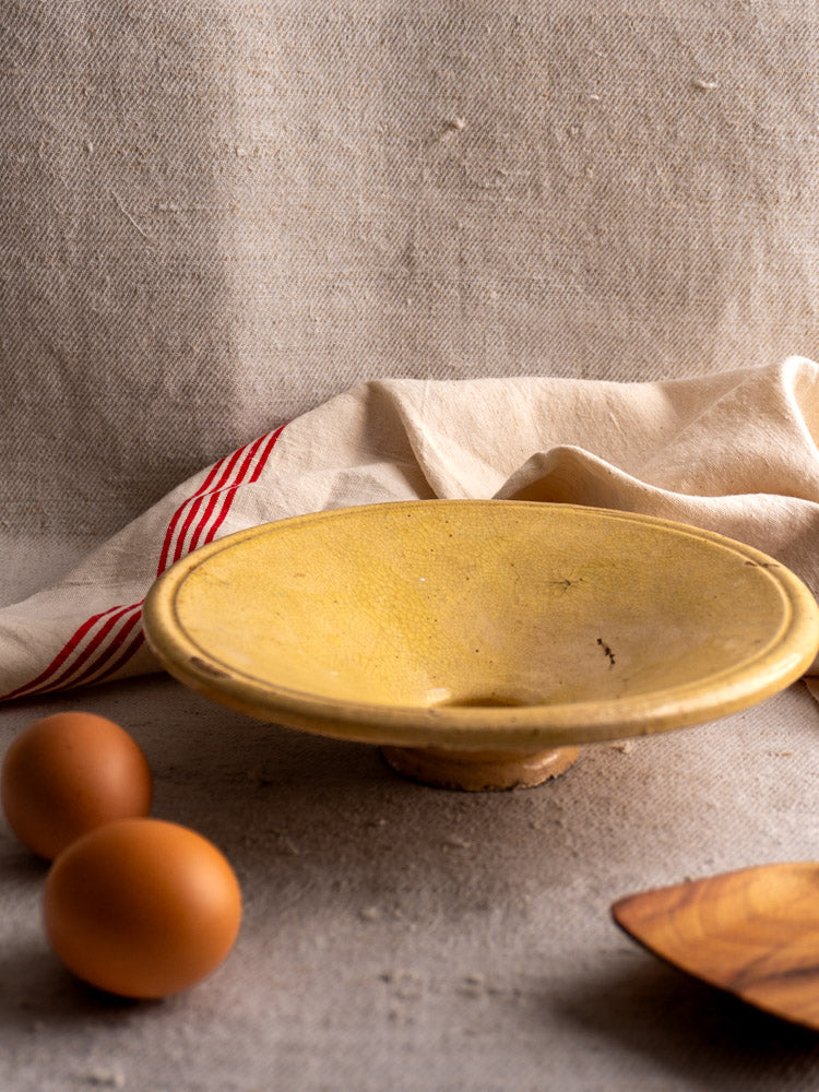 Antique French Tourne Omelette plate in Provencal yellow ochre earthenware with brown eggs on a beige surface.