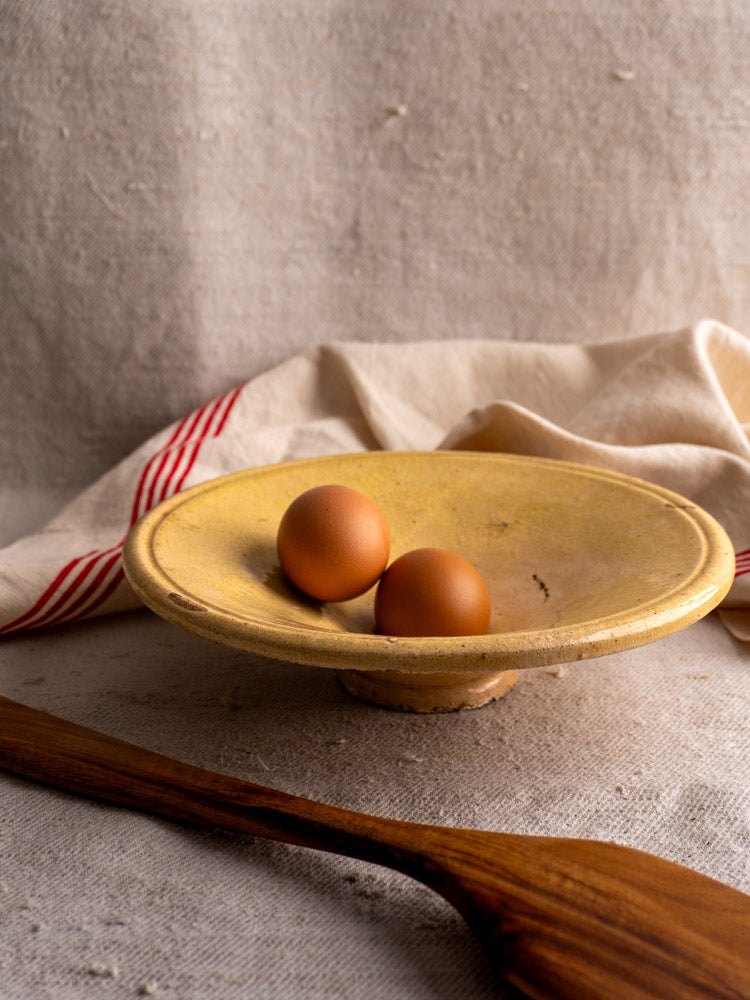 Antique French omelette plate in yellow ochre earthenware with two brown eggs, red-striped cloth background, late 19th century.