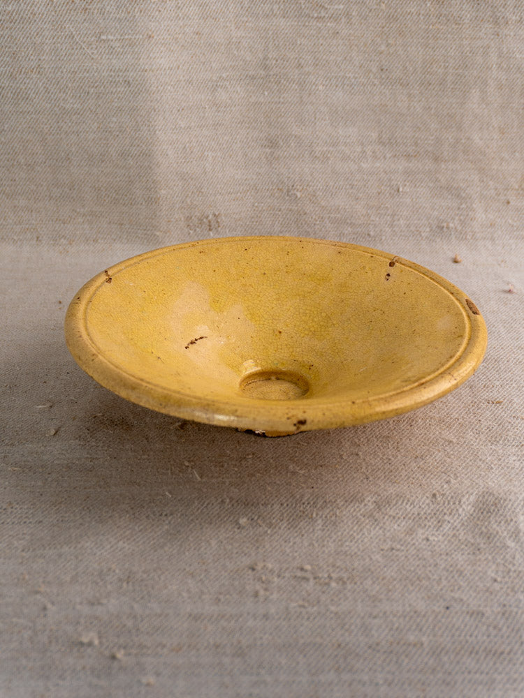 Antique French Tourne Omelette plate in yellow ochre earthenware, shallow form, on rustic beige fabric background.