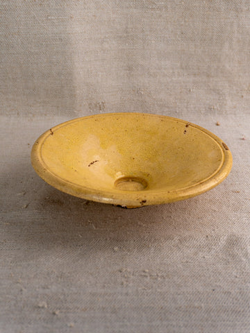 Antique French Tourne Omelette plate in yellow ochre earthenware, shallow form, on rustic beige fabric background.