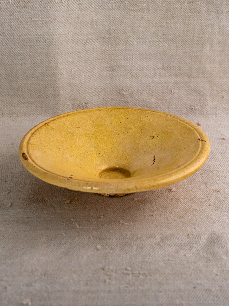 Antique French Tourne Omelette plate in yellow ochre earthenware with central hole, displayed on textured beige fabric.