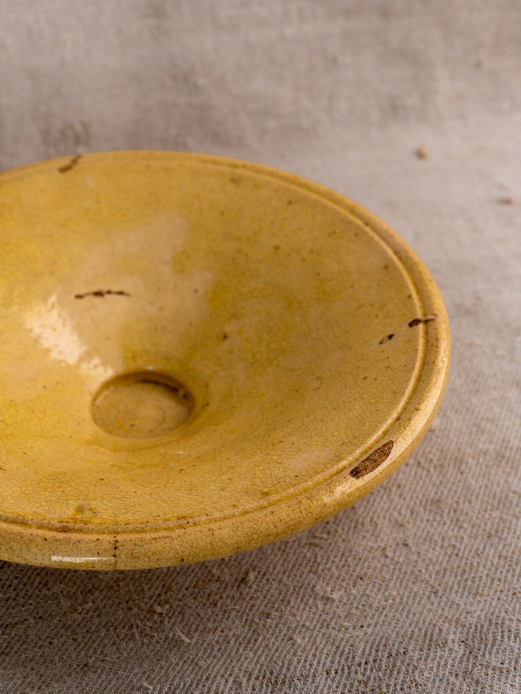 Antique French Tourne Omelette plate in yellow ochre earthenware with central dip and small chips on textured beige fabric.