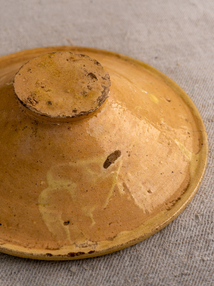Antique French Tourne Omelette lid in yellow ochre earthenware with round knob and patina, on coarse gray fabric.