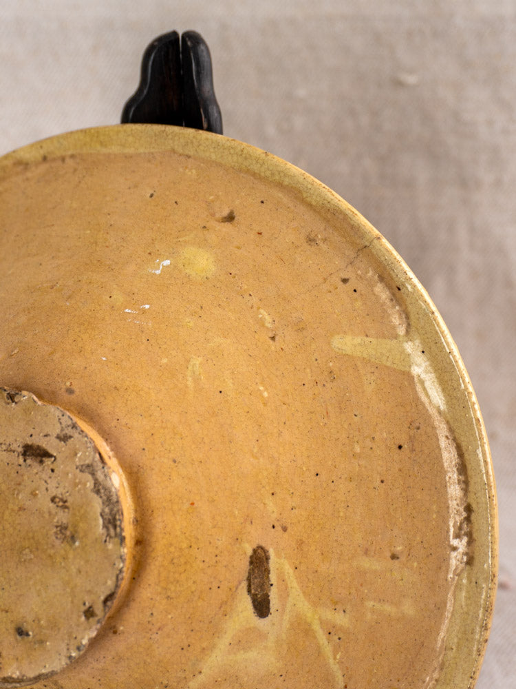 Antique French Tourne Omelette plate underside in yellow ochre earthenware, visible foot ring, textured surface, on neutral fabric.