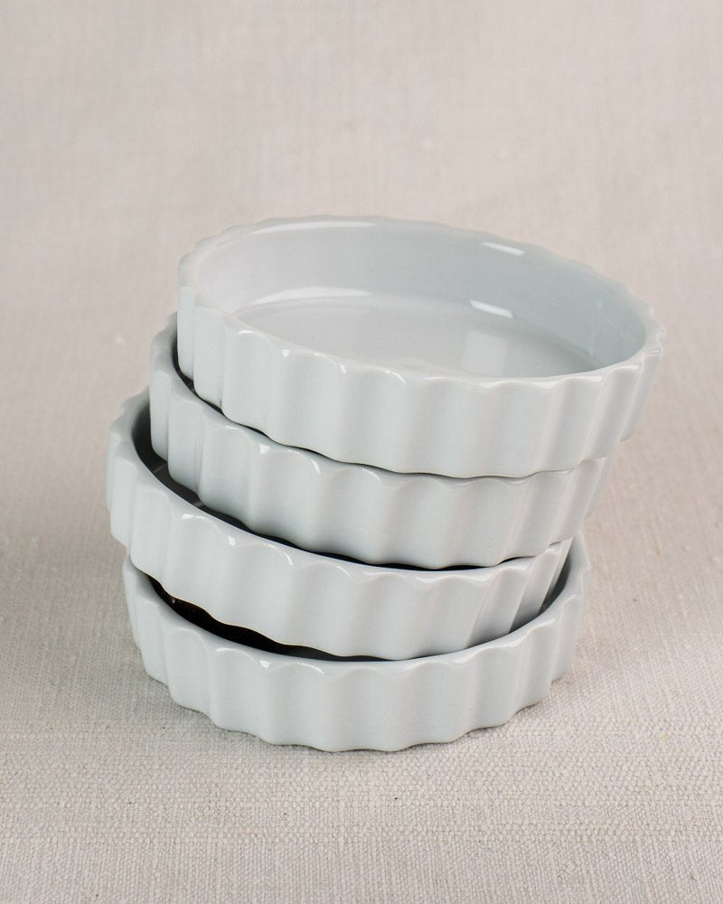 Set of four white fluted porcelain Vintage French CNP quiche dishes stacked on beige textured surface.