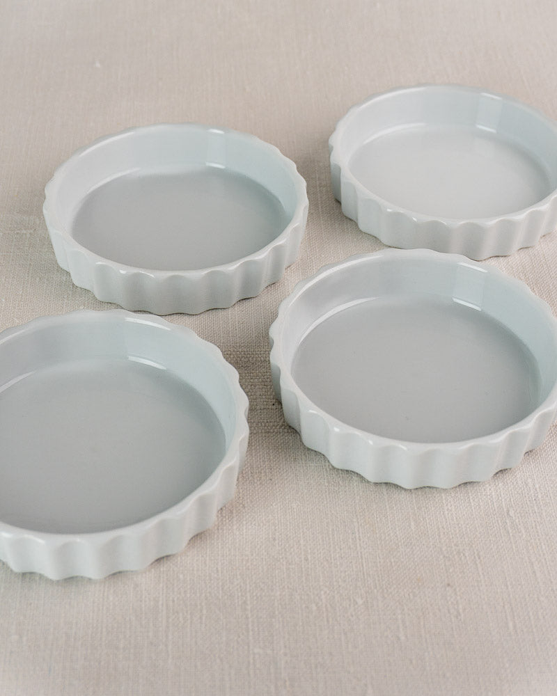 Set of four vintage French CNP white fluted porcelain quiche dishes on beige fabric.