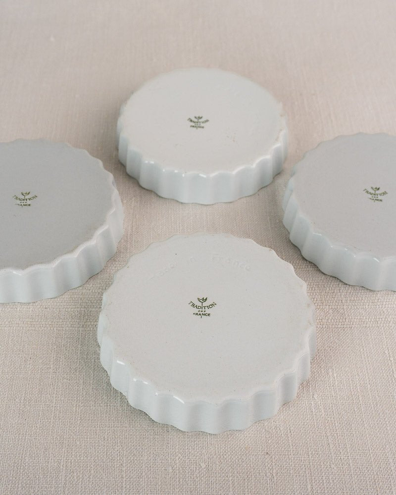 Set of four fluted white porcelain coasters with scalloped edges, French quiche dish inspired, on light fabric.