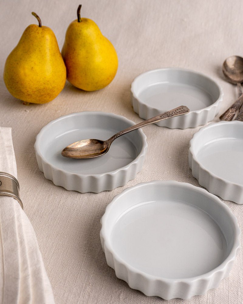 Set of four vintage French fluted white porcelain quiche dishes with silver spoon and pears.