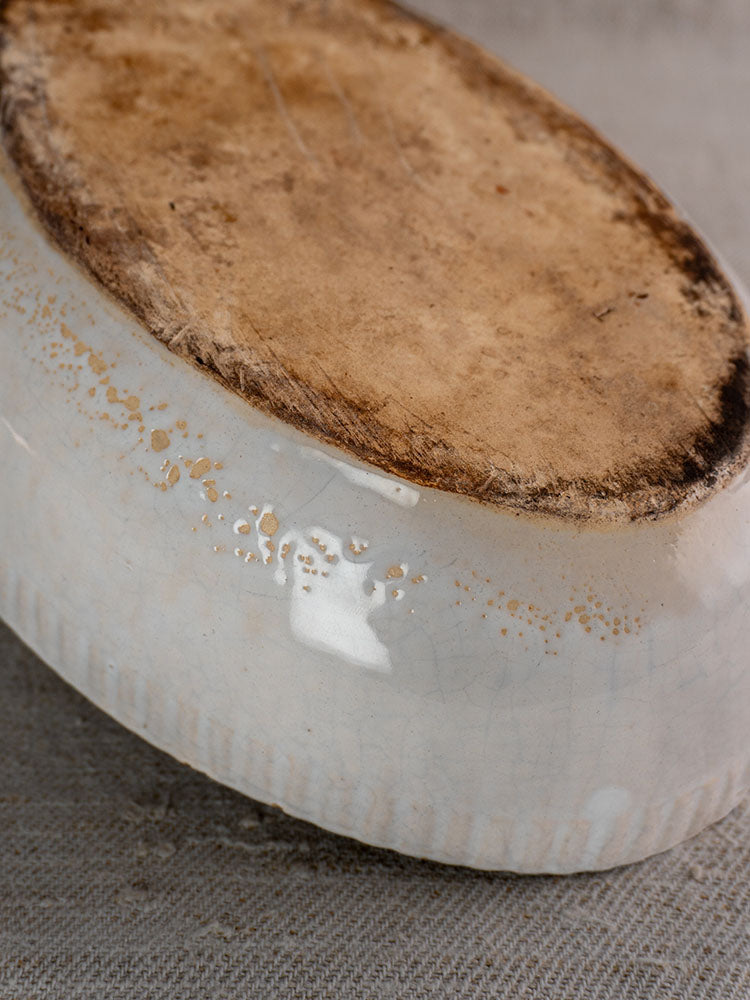 Antique French gratin dish base with worn, unglazed earthenware and discoloration on neutral fabric backdrop.