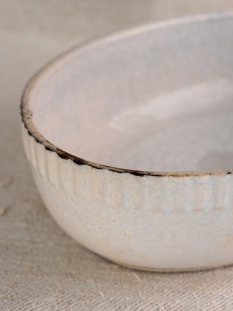 Antique French gratin dish, early 20th-century glazed earthenware with textured white finish and dark rim on beige fabric.