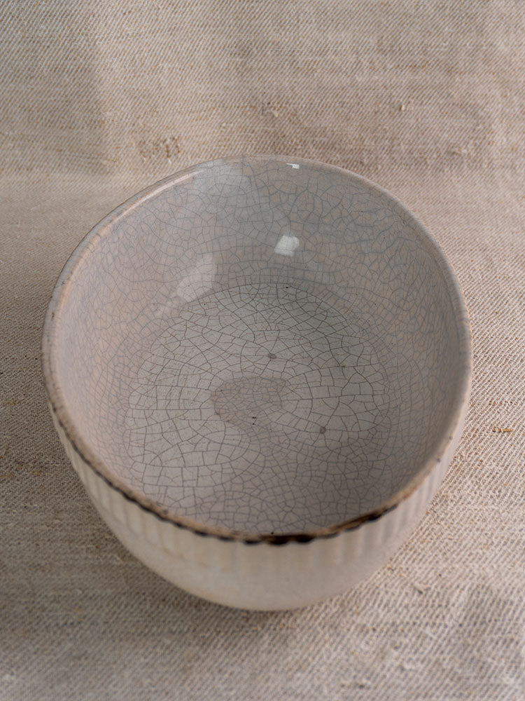 Antique French glazed earthenware gratin dish with crackled off-white glaze and brown edges on beige textured fabric.