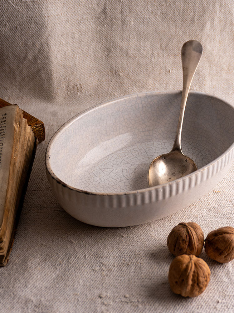 Antique French earthenware gratin dish on beige cloth with walnuts and vintage book for farmhouse kitchen decor.