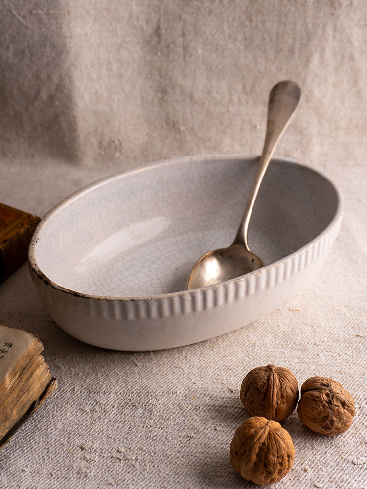 Antique French glazed earthenware gratin dish with crackled white finish and ridged sides on beige fabric.