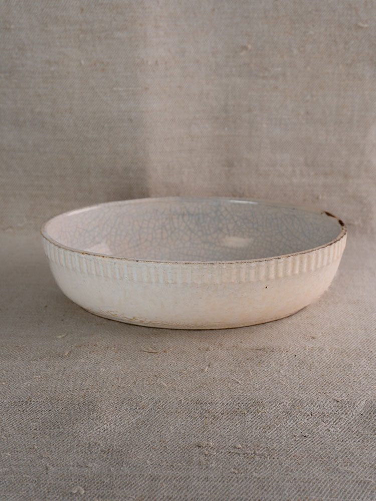 Early 20th-century French glazed earthenware gratin dish with ribbed edge and light crackle, on beige linen fabric.
