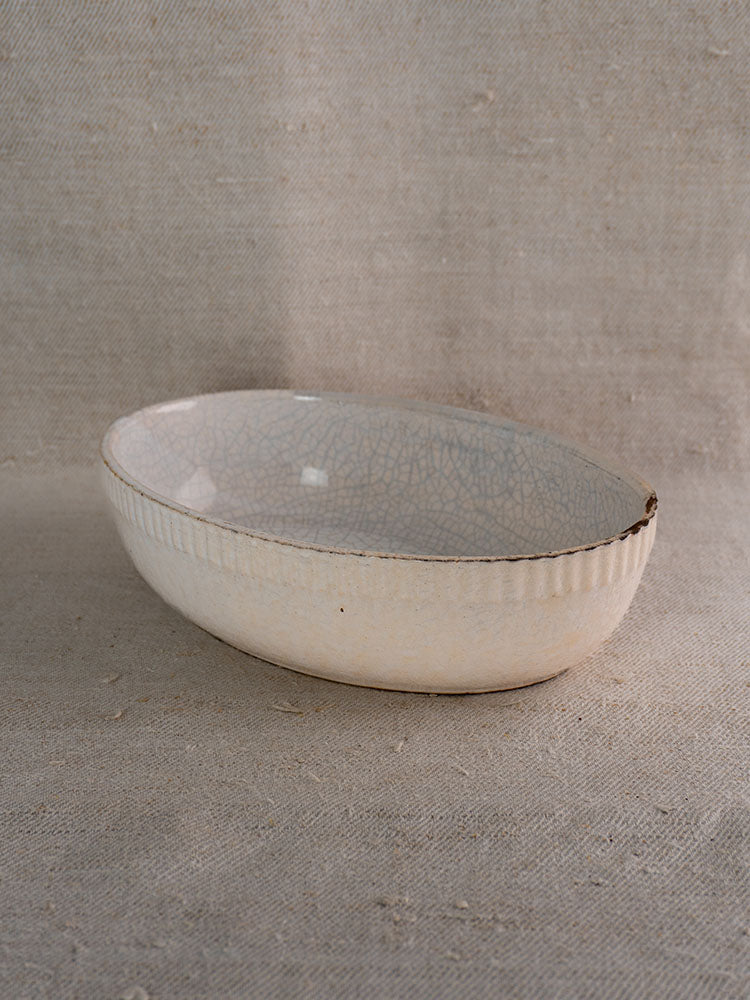 Antique French glazed earthenware gratin dish, early 20th century, ribbed sides, crackle glaze, on beige textured fabric.