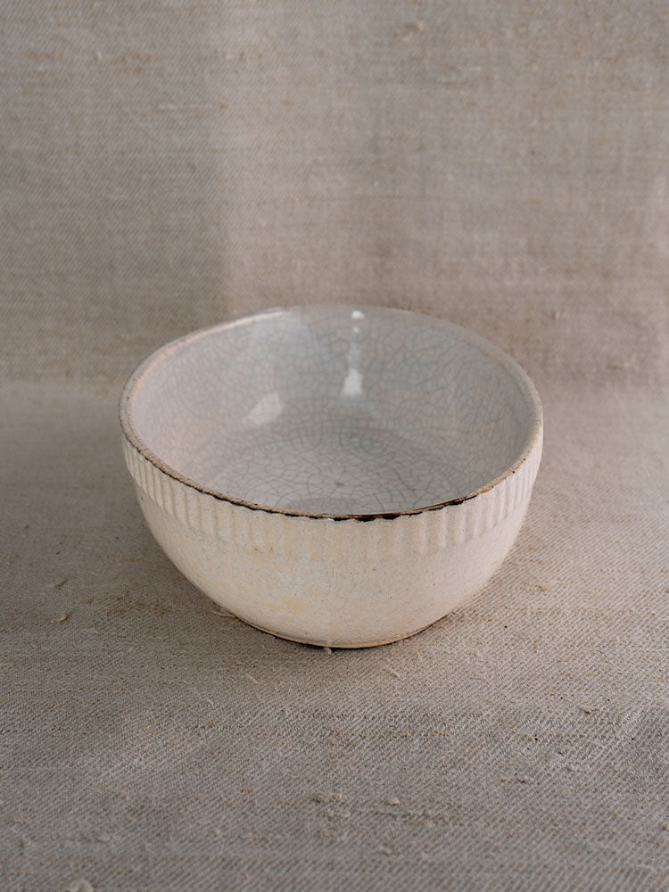 Handmade antique French glazed earthenware gratin dish with light crackle and vertical ridges, on beige textured fabric.