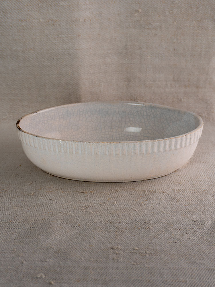 Antique French glazed earthenware gratin dish with crackled finish and vertical ridged rim on woven fabric background.