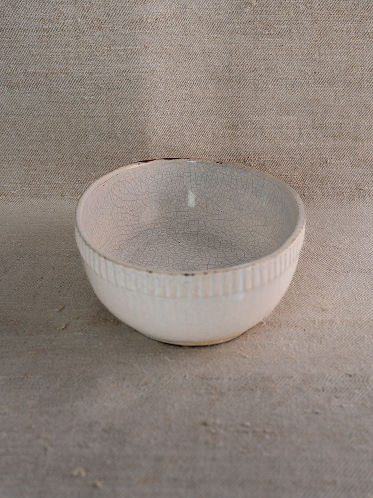 Antique French earthenware gratin dish with glazed finish and ribbed rim, on textured beige fabric.