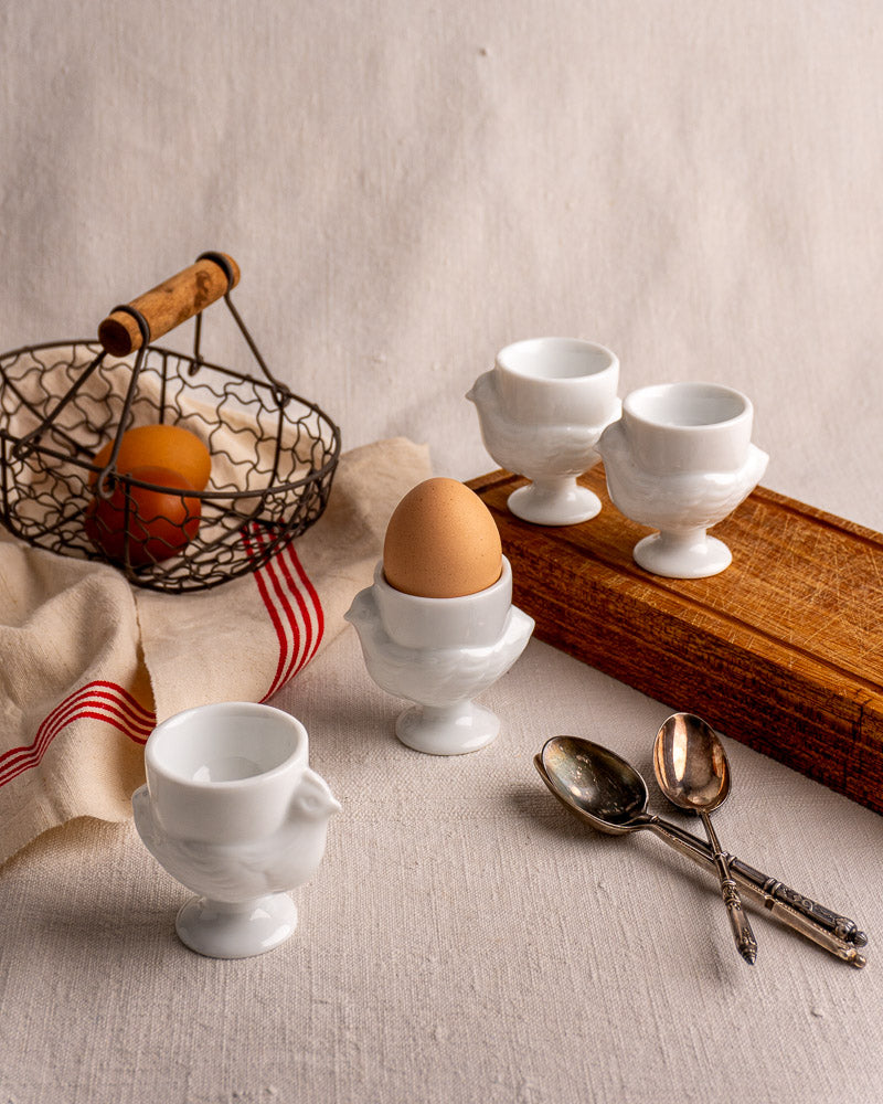 Set of four vintage French opaline glass hen egg cups with classic wing and tail details on neutral surface.